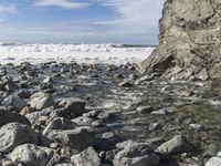 an image of rocks in water on shore line with sky and clouds in background in the foreground