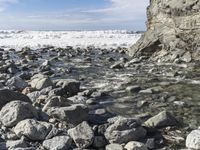 an image of rocks in water on shore line with sky and clouds in background in the foreground