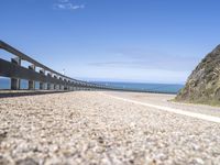 a road with gravel on both sides next to a cliff and blue sky with clouds