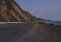 the road going down to the water by the mountains and cliffs, during the evening time