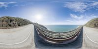 an ocean and two road curves in a fish eye lens shot of a sunny day