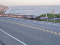 a man is riding a bike on a highway that leads to a cliff with a view of the ocean