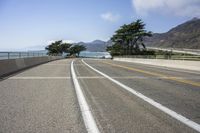 a paved roadway on a mountain side overlooking the ocean with a car driving near by