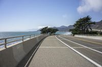 a paved roadway on a mountain side overlooking the ocean with a car driving near by