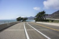 a paved roadway on a mountain side overlooking the ocean with a car driving near by