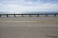 a long bench is sitting in the middle of a highway with ocean in the background