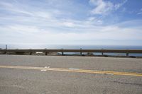 a long bench is sitting in the middle of a highway with ocean in the background