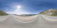 a wide angle fish - eye view of a road next to the sea and rocks