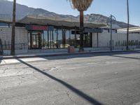 a storefront with mountains in the background and palm trees in front of it,