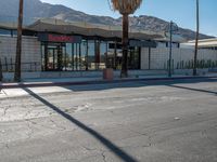 a storefront with mountains in the background and palm trees in front of it,