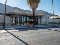 a storefront with mountains in the background and palm trees in front of it,