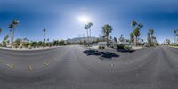 a street with cars and palm trees on both sides in the desert with a sun and sky in the background