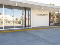 a building with a sidewalk next to it on a sunny day, showing the entrance