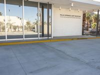 a building with a sidewalk next to it on a sunny day, showing the entrance