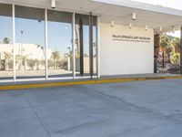 a building with a sidewalk next to it on a sunny day, showing the entrance