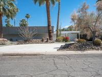 a desert home is shown with many shrubs in the front yard and a street corner