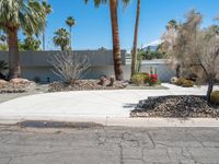 a desert home is shown with many shrubs in the front yard and a street corner