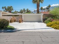 this white home is located with several palm trees and landscaping around it, along the curb