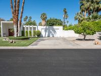 a house with palm trees, a white fence and a driveway that leads to a private entrance