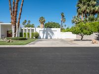 a house with palm trees, a white fence and a driveway that leads to a private entrance