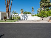 a house with palm trees, a white fence and a driveway that leads to a private entrance