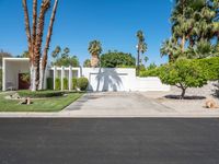 a house with palm trees, a white fence and a driveway that leads to a private entrance