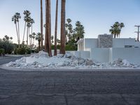 white building with palm trees and rocks surrounding it on an empty street surface with a gray truck in the distance