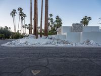 white building with palm trees and rocks surrounding it on an empty street surface with a gray truck in the distance