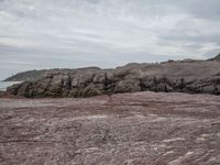 a man standing on top of a red mountain in front of a cliff with a surfboard