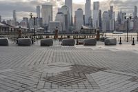 a paved park with benches next to a water body and a skyline of high rises in the background
