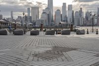 a paved park with benches next to a water body and a skyline of high rises in the background