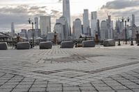 a paved park with benches next to a water body and a skyline of high rises in the background