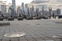 a paved park with benches next to a water body and a skyline of high rises in the background