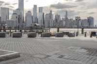 a paved park with benches next to a water body and a skyline of high rises in the background