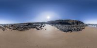 a panorama of a beach and some rocks near the ocean with the sun rising in the background