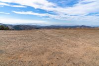 desert area with sparse brown ground and blue sky in background with clouds and mountain views