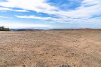 desert area with sparse brown ground and blue sky in background with clouds and mountain views