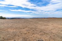 desert area with sparse brown ground and blue sky in background with clouds and mountain views