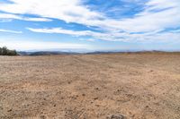 desert area with sparse brown ground and blue sky in background with clouds and mountain views