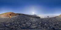 a panorama camera of a mountain side trail with sun shining above it and snow capped peaks