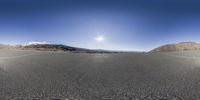 panoramic shot of a road with no traffic visible in it with sun and mountain range