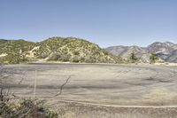 a view along a dirt road of an empty field and mountains in the distance of the scene