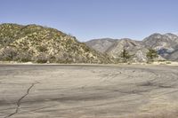 a view along a dirt road of an empty field and mountains in the distance of the scene