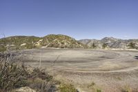 a view along a dirt road of an empty field and mountains in the distance of the scene