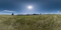 a 360 - lens panorama image of a large grassy field, a windmill pole and many trees in the back ground