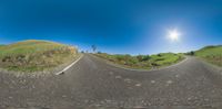 a 360 - view photograph taken of a street, grass and dirt area with mountains in the distance