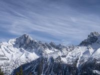 a mountain range with snow on top and some clouds in the background and a bright blue sky overhead