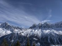 a mountain range with snow on top and some clouds in the background and a bright blue sky overhead