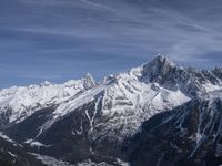 a mountain range with snow on top and some clouds in the background and a bright blue sky overhead