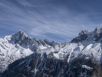 a mountain range with snow on top and some clouds in the background and a bright blue sky overhead